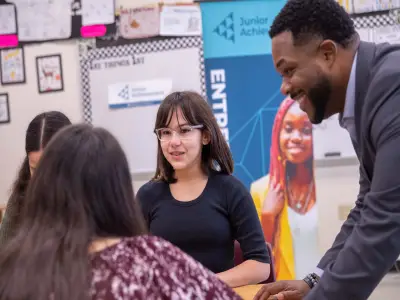 Image of young people in a classroom smiling and talking with an adult